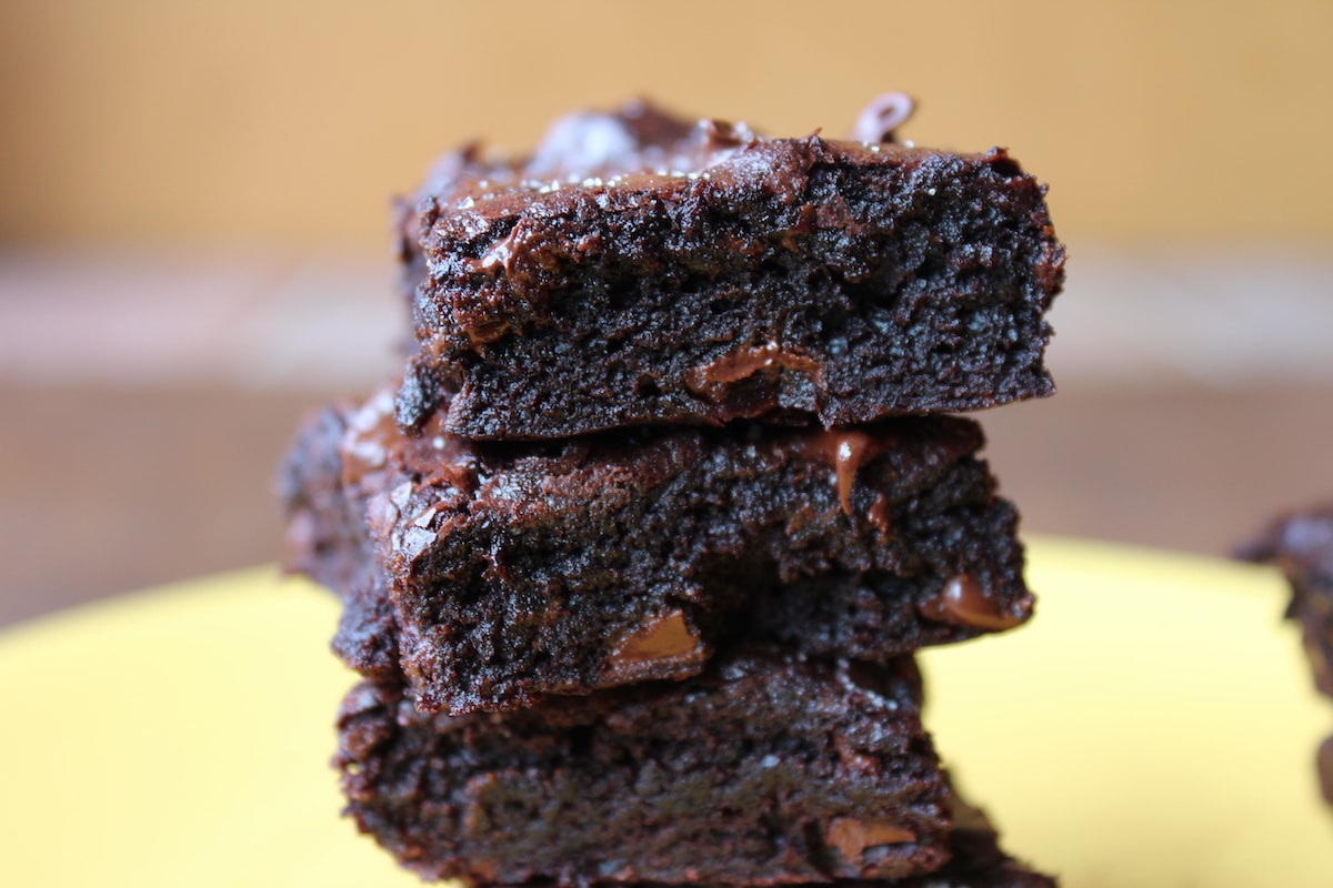 Three dark chocolate brownies stacked on a yellow plate