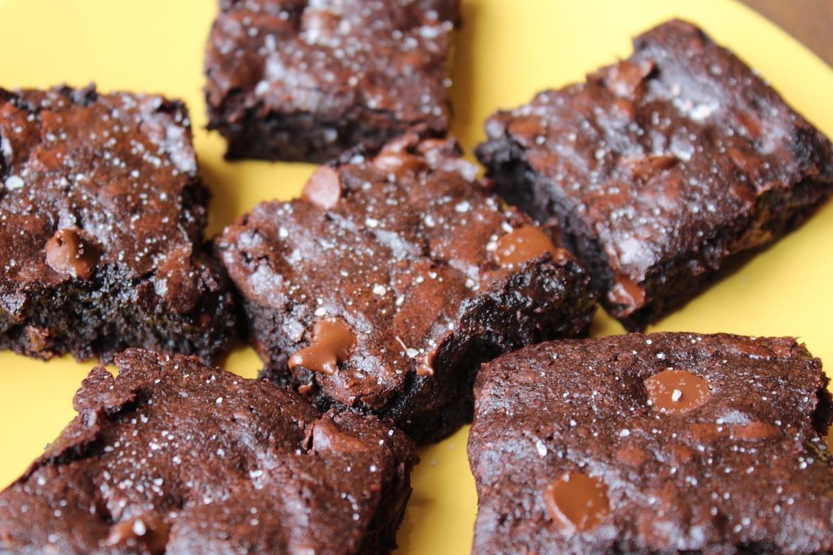 Several brownies on a yellow plate with visible chocolate chips and flaky sea salt