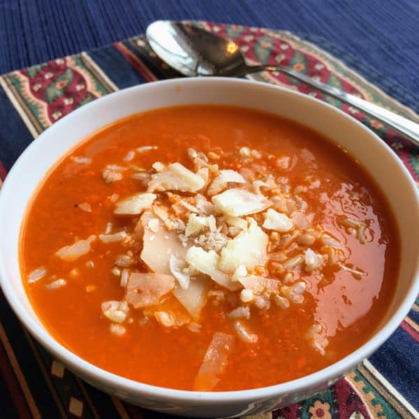 Bowl of creamy tomato soup with rice and parmesan, with a spoon, on a blue printed placemat