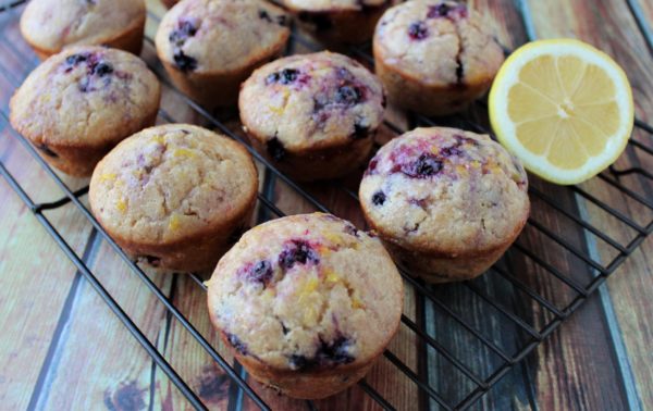 Many lemon blueberry muffins and a half lemon on a cooling rack