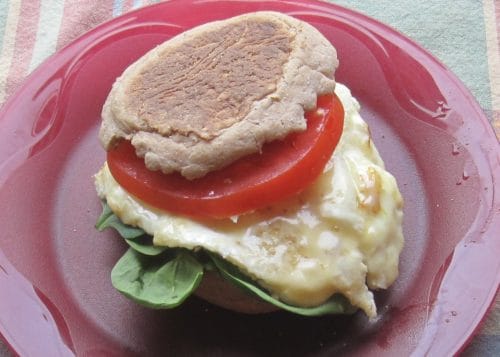 Classic fried egg sandwich on a plate, layered with a tomato slice and greens.