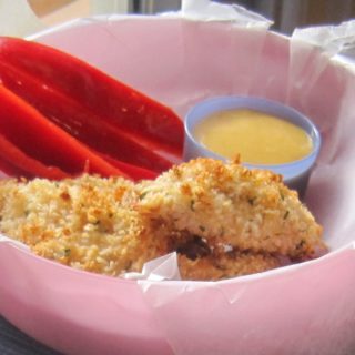 Pink bowl lined with wax paper, holding panko chicken chunks, red bell pepper strips, and honey mustard sauce.