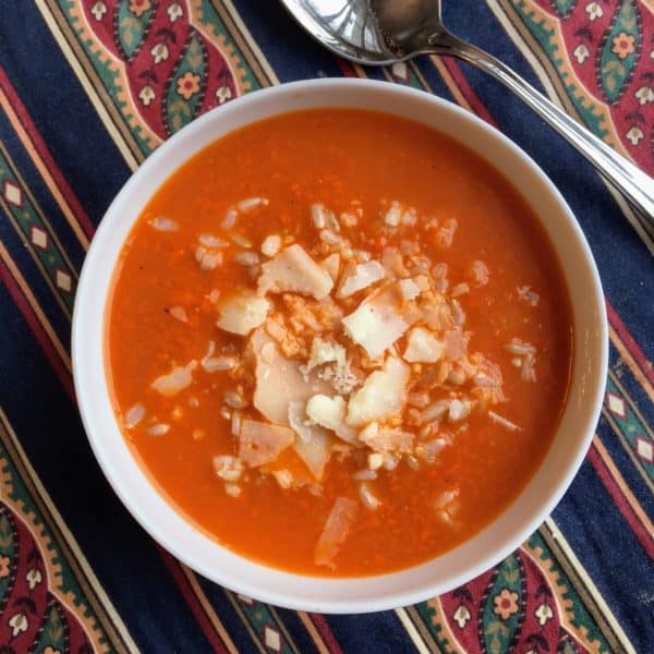 overhead view of tomato rice soup in a white bowl with a spoon next to it