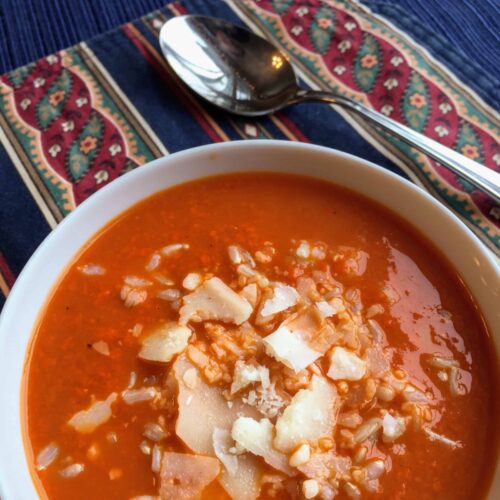 Tomato rice soup with saved parmesan in a white bowl, on a blue printed placemat