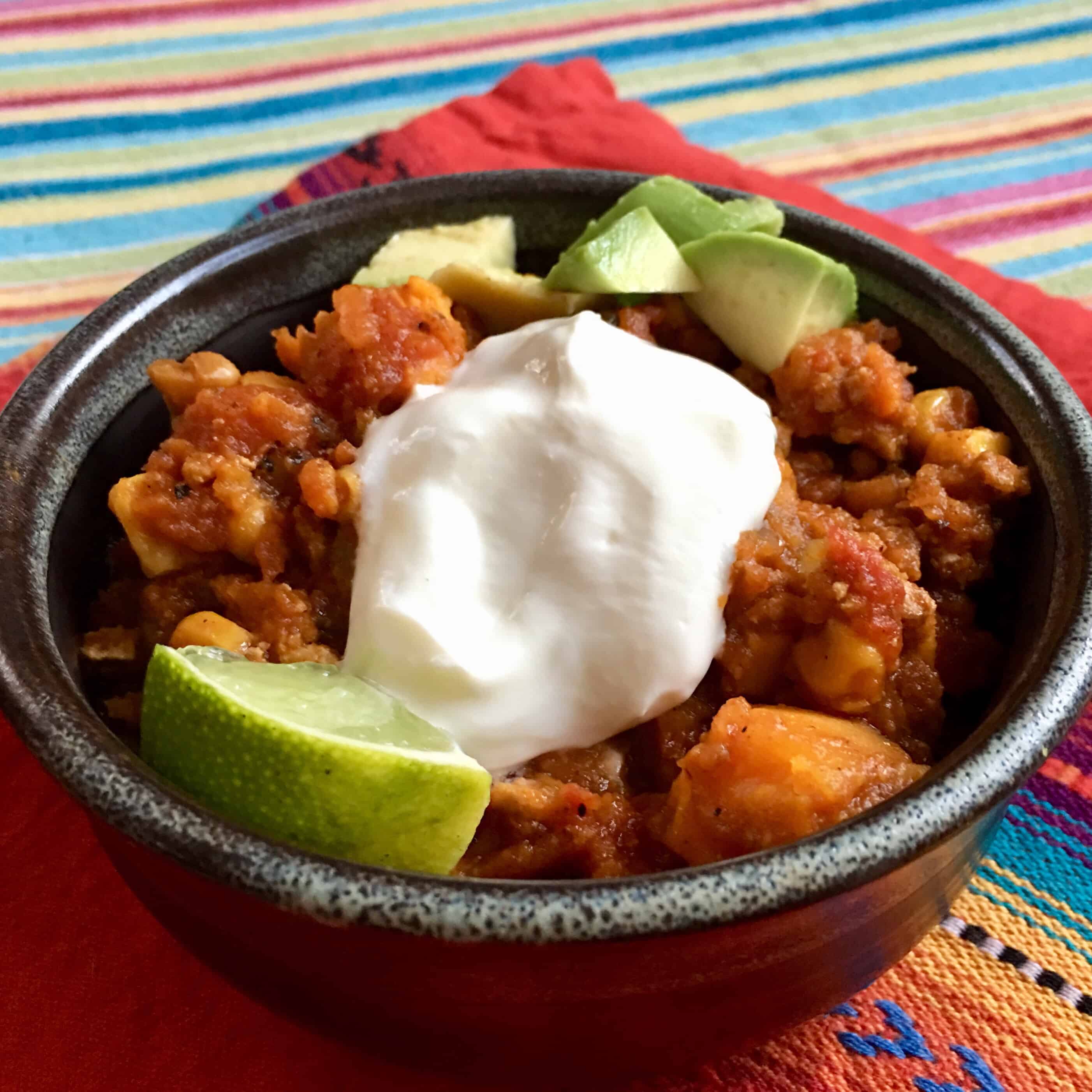 A single serving of Autumn Harvest Chili topped with plain yogurt and a lime wedge. 