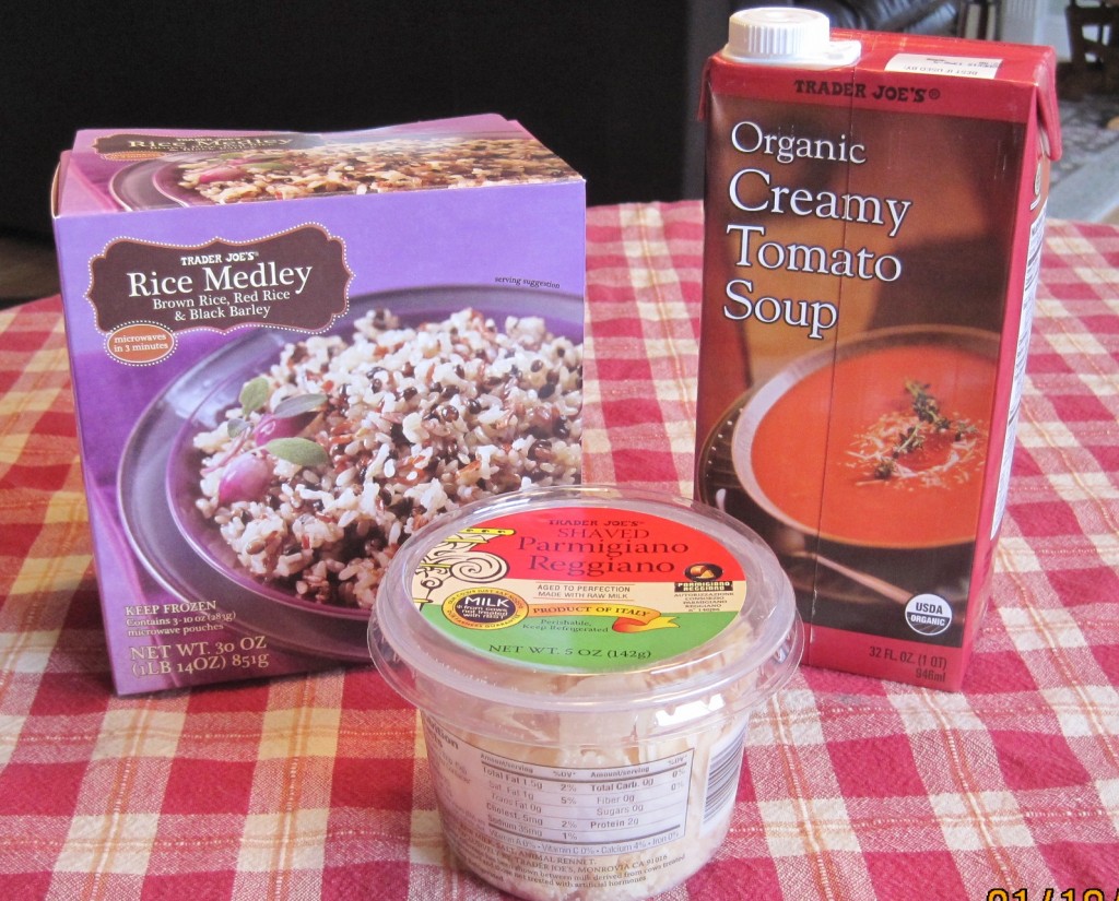 A box of Trader Joe's frozen rice, a container of organic creamy tomato soup, and a container of shaved parmesan cheese, on a red checked tablecloth
